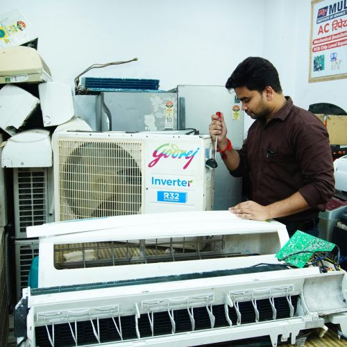 Technician repairing an air conditioner unit in New Delhi workshop.