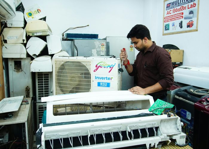 Technician repairing an air conditioner unit in New Delhi workshop.